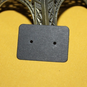 Detail of a black kraft paper earring display card leaning against a metal Eiffel Tower model