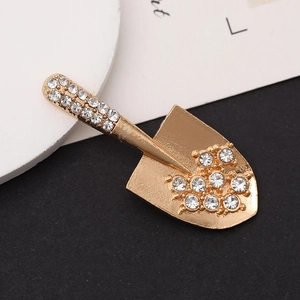 Golden shovel-shaped brooch with white rhinestones on a textured background