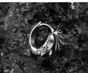 Macro shot of silver vintage dragon-head earring with wings on dark rock background