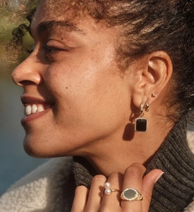 Close-up of golden earrings with black gemstones and pearl rings on model in soft light