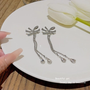 Detail of silver bow tassel earrings with crystals and water drop pendants on white porcelain