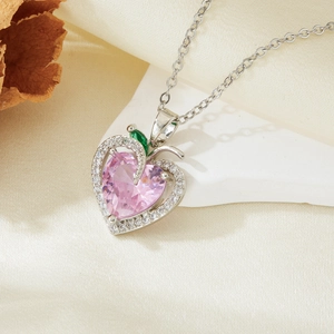 Macro shot of silver heart necklace with pink gem and green leaf detail on silk