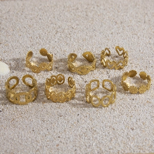 Set of seven golden stainless steel open rings with daisy and heart designs on sand