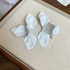 Close-up of white matte flower earrings on a linen jewelry tray with petal texture