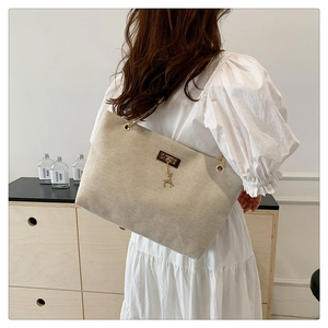 Detail of beige tote bag featuring golden chain straps and a small deer charm accessory