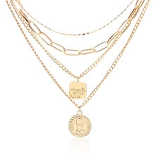 Close-up of gold layered chain necklace with portrait relief and square engraved pendant