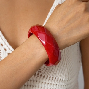 Close-up of a wide red acrylic resin bangle with wavy faceted texture on a model's wrist