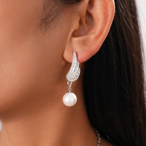 Detailed view of silver wing earrings with inlaid crystals and a white pearl drop pendant