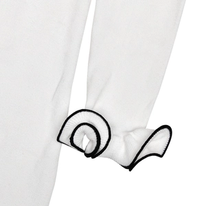 Detailed close-up of white knitted sleeve with elegant black edge ruffle trim design