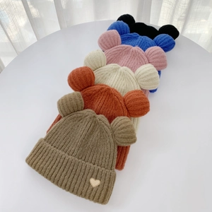 Detail of multi-color knitted beanies with cute bear ears and heart patch on white background