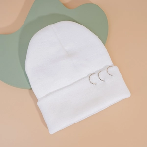 Détail du bonnet en maille blanche avec trois anneaux métalliques argentés sur le rebord