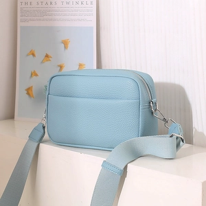 Detail of light blue litchi pattern leather camera bag with wide fabric shoulder strap