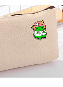 Close-up of a green cartoon frog astronaut enamel pin on a beige canvas school bag