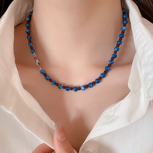 Detail of blue jade beaded necklace with red spacers on model wearing a white shirt