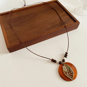 Détail du pendentif feuille sur base bois avec collier en cordon tressé marron