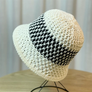 Detail of color-block woven straw bucket hat with black V-pattern on beige texture