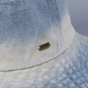 Detail of gradient blue denim bucket hat with frayed edges and metallic logo plaque