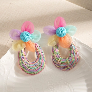 Close-up of hand-woven raffia flower earrings with tulle on a white embossed plate