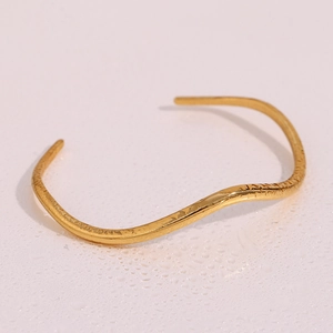 Minimalist gold wavy open bangle with hammered texture on a soft pink background with water drops