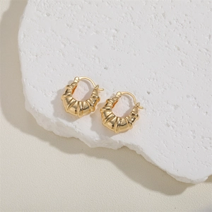 Macro shot of gold croissant dome hoop earrings placed on a white textured stone base