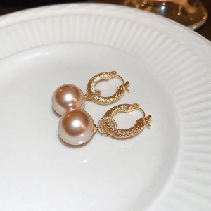 Detalle de pendientes de aro dorados con perlas grandes color champán en plato cerámico