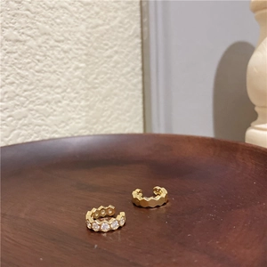 Détail de boucles d'oreilles dorées en nid d'abeille avec zircons sur plateau bois