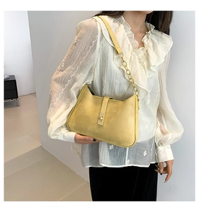 Detail of yellow suede shoulder bag featuring gold chain strap and metallic lock closure