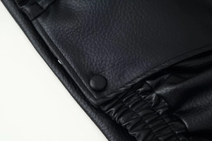 Detail of black pebbled leather texture with snap buttons and elastic cuffs on a jacket