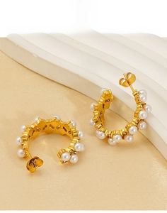 Detail of C-shaped gold titanium steel earrings with white pearls and crystals