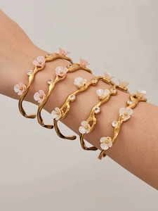 Close-up of five stacked gold flower bangles with pink enamel and crystals on a wrist