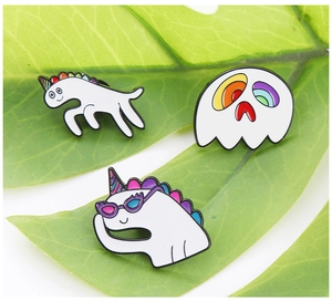 Detail of three white enamel unicorn badges with rainbow mane on a green leaf background