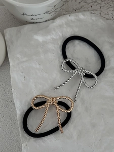 Set of gold and silver twisted metal bow hair ties on a white textured stone background