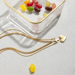 Close-up of double-layer gold necklace with heart and cross pendants on gray surface