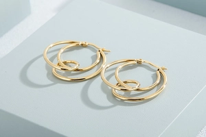 Macro shot of gold-plated geometric triple layered circle knot earrings on blue grey background