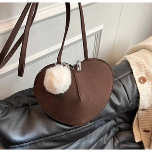 Detail der herzförmigen braunen Wildleder-Umhängetasche mit flauschigem weißem Bommel