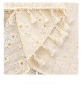 Close-up of white cotton linen tablecloth featuring daisy embroidery and tassel edges