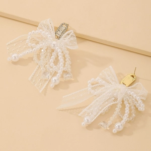 Détail de boucles d'oreilles nœud en dentelle avec perles et zircon sur fond beige