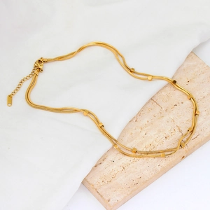 Detail of 18K gold double layer snake chain necklace on white silk and travertine