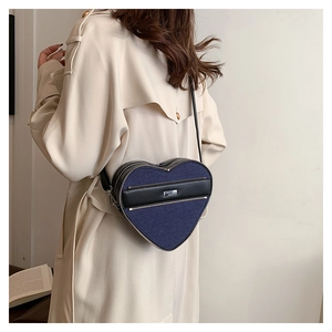 Detail of heart-shaped crossbody bag featuring denim fabric and leather accents on model