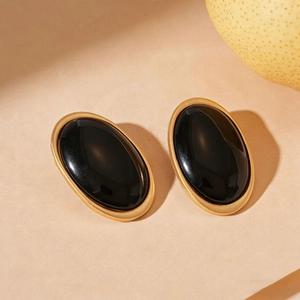 Close-up of vintage oval resin earrings in black with gold metal trim on beige background