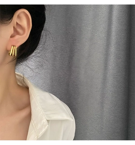 Close-up of triple-layered golden geometric hoop earrings worn by a model in detail