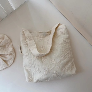 Detail of floral embroidery on beige canvas tote bag with matching hair scrunchie accessory