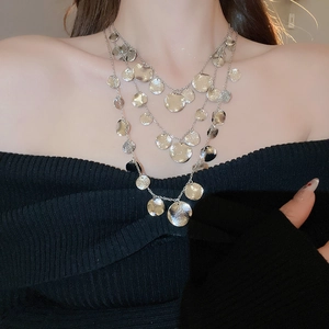 Detail of layered silver necklace featuring hammered round metal pendants on a black knit top
