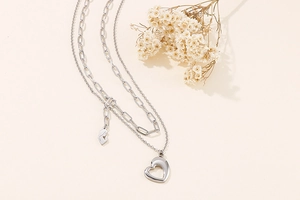 Detail of silver double-layered necklace with heart pendant and abstract face tag