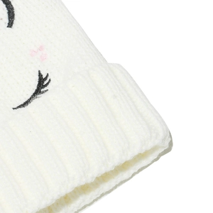 Détail du bonnet blanc en tricot avec cils de licorne brodés et touches de rose