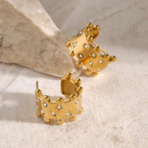 Detail of 18k gold C-shaped earrings with white zircons and beaded edge on stone background