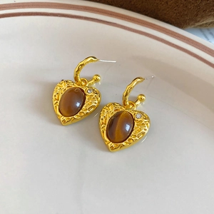 Detailed view of heart-shaped gold earrings with brown tiger eye stone and diamond accents
