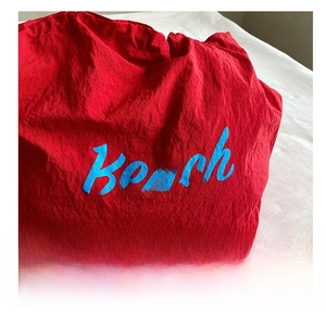 Detail of red wrinkled fabric tote bag featuring blue Beach embroidery and soft texture