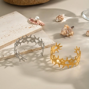 Artistic detail of gold and silver textured geometric open bangles on stone with sea shells