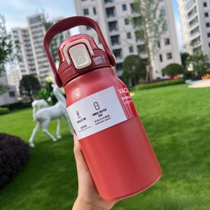 Handheld red insulated stainless steel bottle with straw and handle on green grass